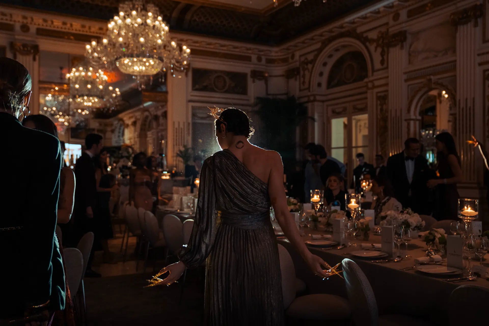 Danseuse en performance. Elle porte une couronne, se tient face aux invités. Plan large avec tables, lustres et dorures en fond.